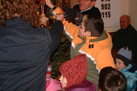 Kinder schmücken einen Christbaum mit den mitgebrachten Bastelarbeiten